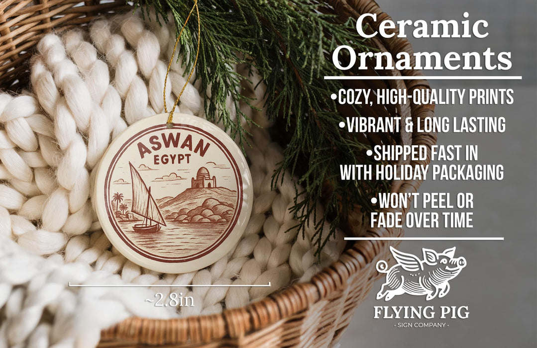 Ceramic ornaments, featuring a round ornament with a sailboat and a castle, are displayed in a basket with greenery.