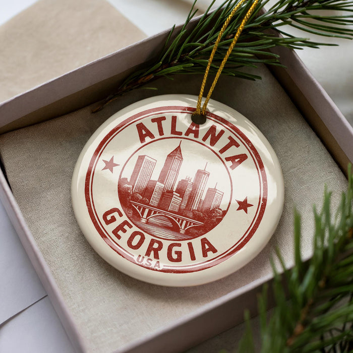 A circular ornament with the text "ATLANTA GEORGIA USA" printed on it, placed inside a box with pine branches.