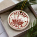 A circular ornament with the text "ATLANTA GEORGIA USA" printed on it, placed inside a box with pine branches.