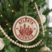 A Christmas tree decorated with ornaments, including a circular ornament with the text "ATLANTA GEORGIA USA" and a wooden bead decoration.