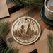 A circular ornament with a Buddha image and the text "AYUTHAYA HISTORICAL PARKTARK THAILAND" is displayed on a wooden surface, surrounded by pine branches and a cup of coffee.