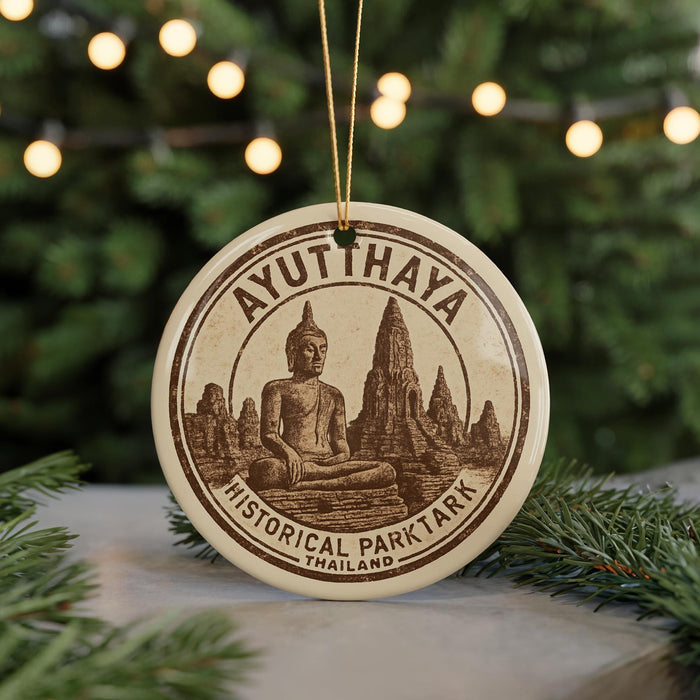 A circular ornament featuring a Buddha statue and the text "AYUTTHAYA HISTORICAL PARKTARK THAILAND" is displayed on a table with pine branches in the background.