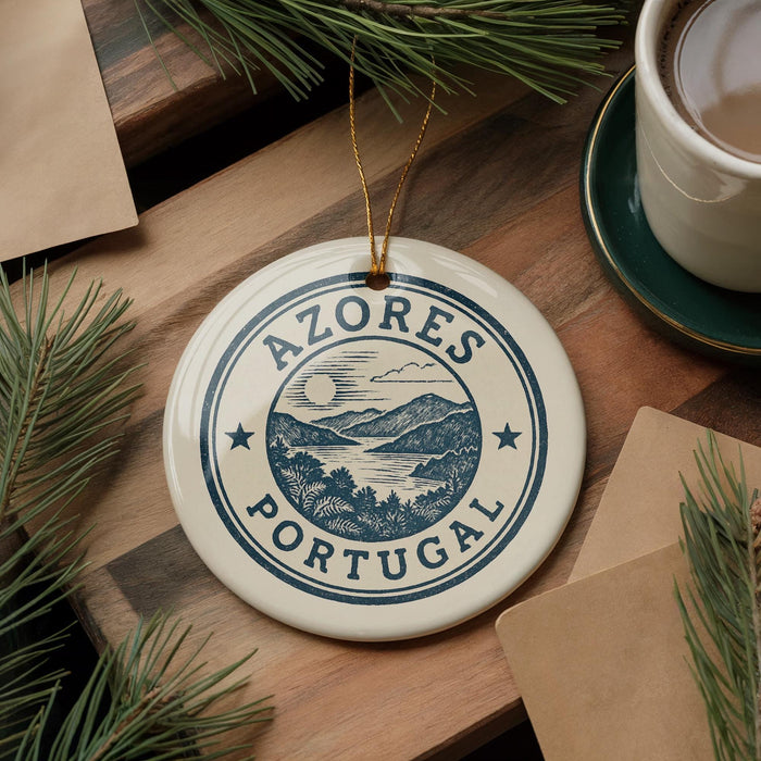 A circular ornament with the text "AZÚRES PORTUGAL" is displayed on a wooden surface, surrounded by pine branches and a cup of coffee.