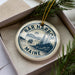 A circular ornament with the text "BAR HARBOR MAINE" printed on it, surrounded by a pine branch and pine needles.