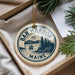 A circular ornament with the text "Bar Harbor Maine" printed on it, hanging from a string.