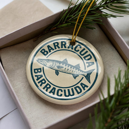 A circular ornament with the text "BARRACUDA" and a fish illustration, placed in a box with pine branches.