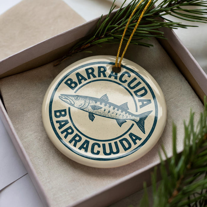 A circular ornament with the text "BARRACUDA" and a fish illustration, placed in a box with pine branches.