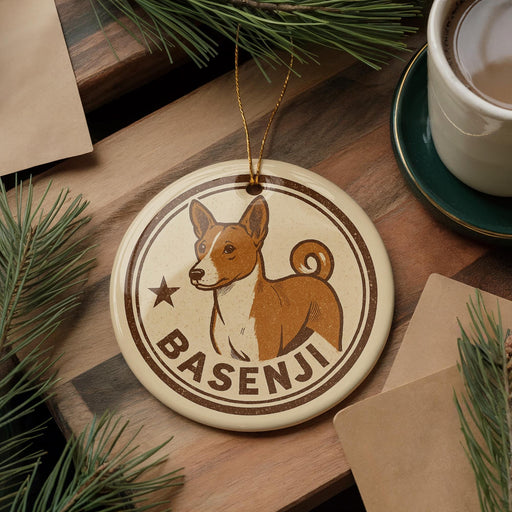 A circular ornament featuring a brown and white dog, with the name "Basesenji" written on it, is displayed on a wooden surface alongside a cup of coffee and some pine branches.