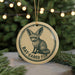 A round ornament featuring a bat-eared fox, with the text "BAT-EARED FOX" printed on it, is hanging from a string in front of a Christmas tree.