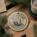 A circular ornament with the text "BATON ROUGE LOUISIANA" and a graphic of a city skyline, hanging on a wooden surface.