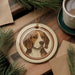 A ceramic ornament featuring a beagle dog is displayed on a wooden surface, surrounded by pine branches and a cup of coffee.