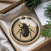A decorative ornament featuring a black and white illustration of a beetle is displayed in a box, surrounded by pine branches.