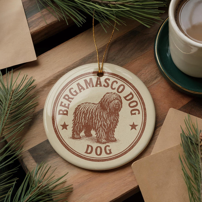 A circular ornament featuring a shaggy dog, likely a Berganco dog, is displayed on a wooden surface alongside a cup of coffee and some pine branches.