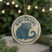 A circular ornament with the text "BINTURONG" and an illustration of a small animal, likely a rodent or rodent-like creature, is displayed in front of a blurred background of Christmas lights.