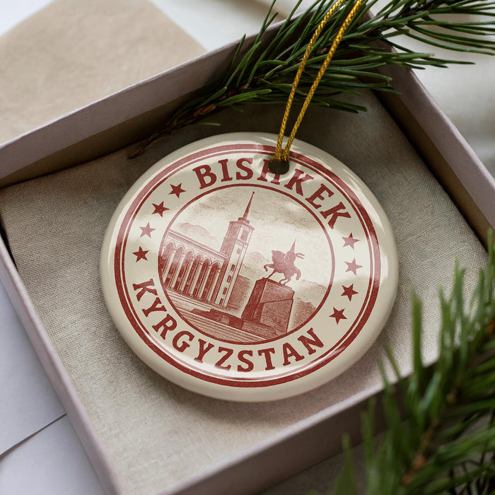 A circular ornament with the text "BISKECK" and "Kyrgyzstan" printed on it, surrounded by a border of stars. The ornament is placed inside a box with pine branches.