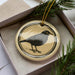 A ceramic ornament in a box, featuring a black bird illustration.