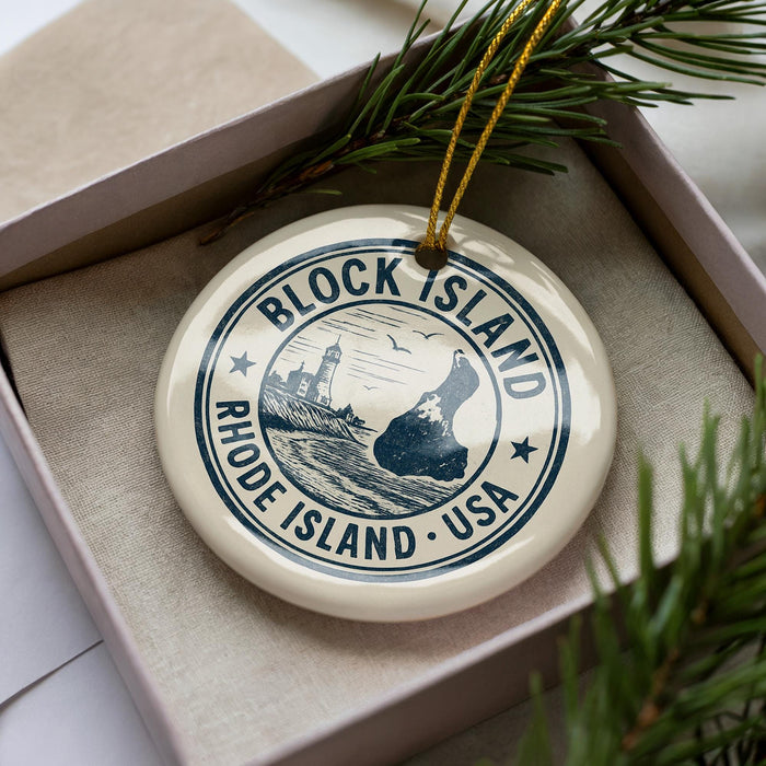 A decorative ornament in a box, featuring a circular design with text and a lighthouse illustration, surrounded by pine branches.