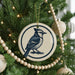 A blue jay ornament is hanging on a Christmas tree, surrounded by ornaments and lights.