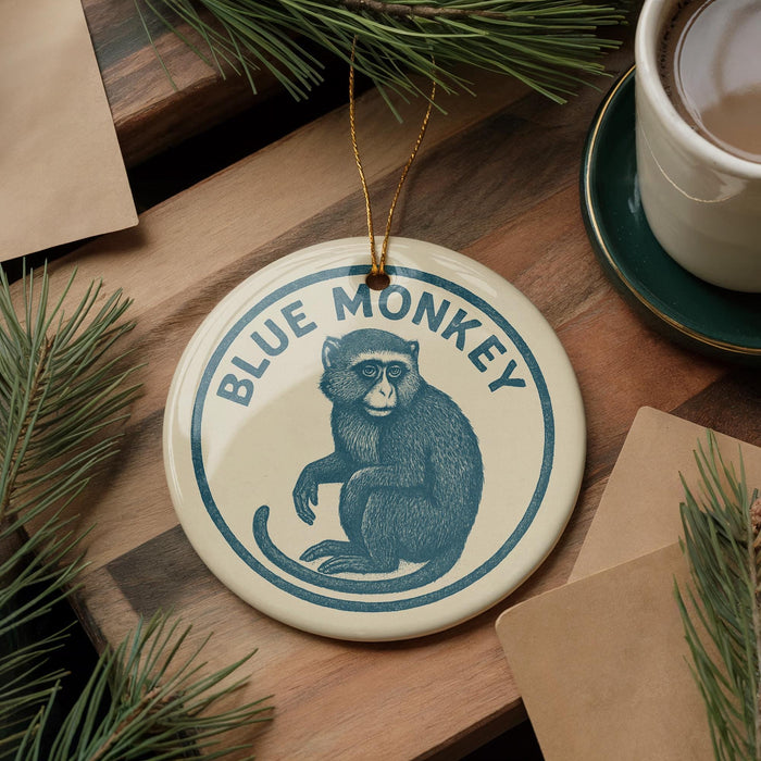 A blue and white ornament featuring a monkey is displayed on a wooden surface, surrounded by pine branches and a cup of coffee.