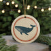 A round ornament featuring a blue whale silhouette is displayed against a blurred background of a Christmas tree with twinkling lights.