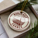 A decorative ornament in a box, featuring a circular design with the text "BORDEAUX FRANCE" and an illustration of a bridge.