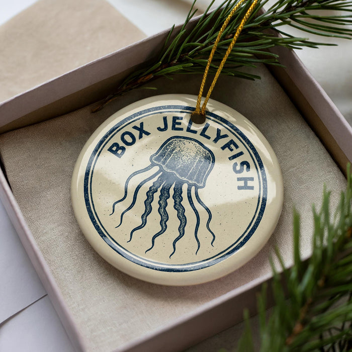 A round ornament with the text "BOX JELLYFISH" and an illustration of a jellyfish is displayed in a box, surrounded by pine branches.