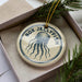 A round ornament with the text "BOX JELLYFISH" and an illustration of a jellyfish is displayed in a box, surrounded by pine branches.