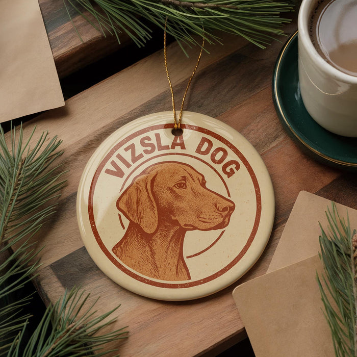 A circular ornament featuring a brown dog's head, with the text "Vizsla Dog" written around it, is displayed on a wooden surface.