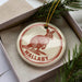 A circular ornament with a kangaroo image and the word "Wallaby" written on it, placed in a box with pine branches.