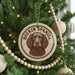 A round ornament with a brown dog's face on it, hanging from a Christmas tree.