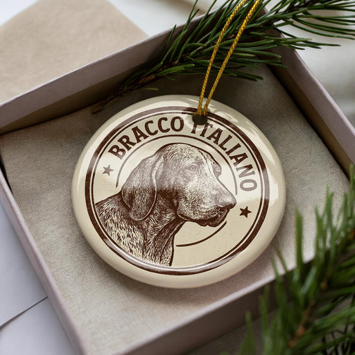 A circular ornament with a dog's head and the text "BRACCO ITALIANO" printed on it, placed inside a box with pine branches.