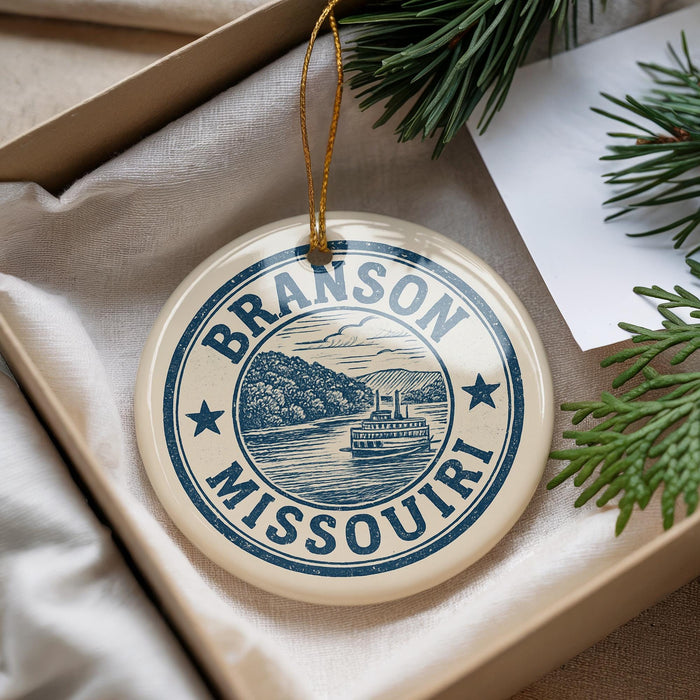 A decorative ornament with the text "BRANSON MISSOURI" and a depiction of a river and boat, hanging from a string.