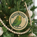 A circular ornament on a Christmas tree featuring a green parakeet, with the word "BUDGERIGAR" written on it.