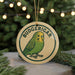 A round ornament with the word "BUDGERIGAR" and a picture of a budgerigar bird, which is a type of parakeet, hanging from a string.