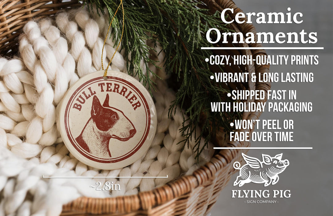 Ceramic ornaments featuring a bull terrier are displayed in a woven basket, with a sprig of greenery nearby.