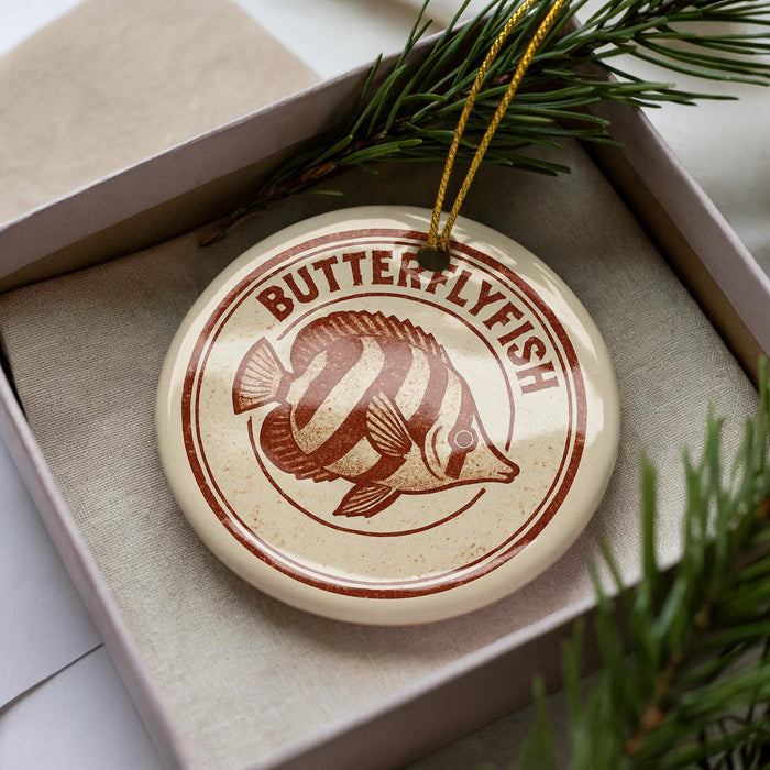 A circular ornament with a butterfly design, placed inside a box with pine branches.
