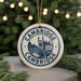 A white ceramic ornament with the text "CAMBRIDGE" and an illustration of a castle or palace, hanging from a string.