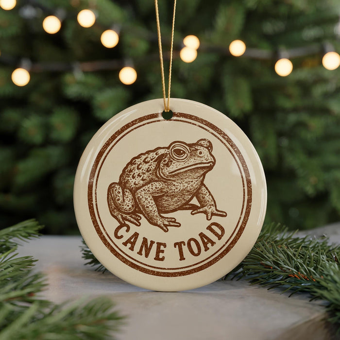 A round ornament with a brown image of a cane toad and the text "CANE TOAD" printed on it, hanging from a string.