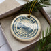 A circular ornament with the text "CANUAN SAINT VINCENT AND THE GREEMENADINES" printed on it, surrounded by pine branches.