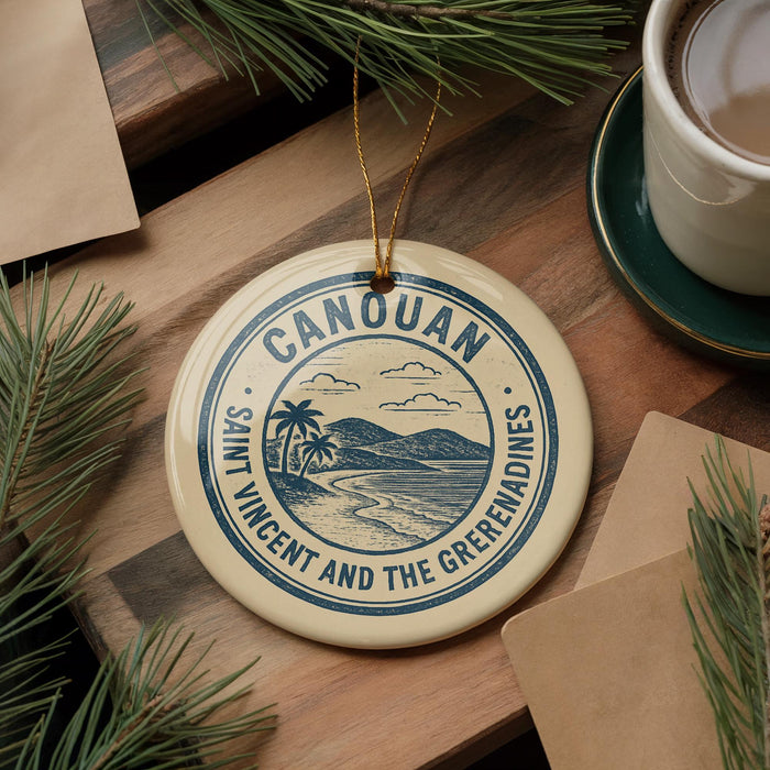 A circular ornament with the text "CANOAN" and "SANT VINCENT AND THE GRETERNADINES" is displayed on a wooden surface, surrounded by pine branches and a cup of coffee.