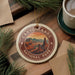 A decorative ornament featuring a scenic image of the Grand Canyon National Park, surrounded by pine branches and a cup of coffee on a wooden surface.