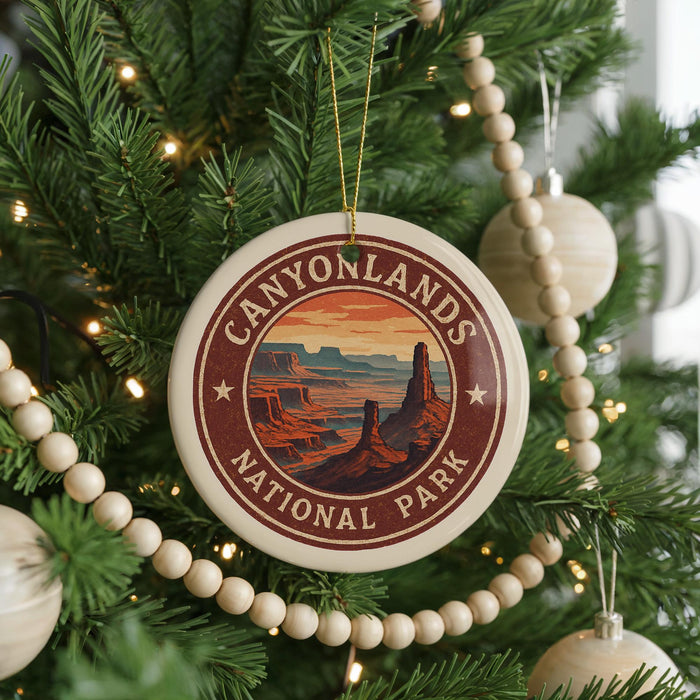 A round ornament on a Christmas tree, featuring a desert landscape with mountains and a sunset, is hanging from a string.