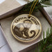 A decorative ornament featuring a monkey is displayed in a box, surrounded by pine branches.