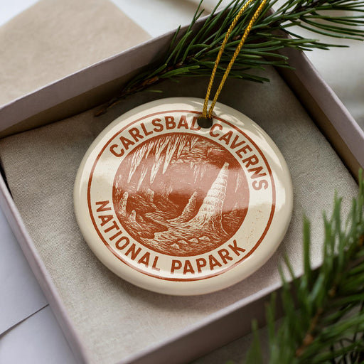 A circular ornament with the text "CARLSBAD CAVENS NATIONAL PAPARK" printed on it, placed in a box with pine branches.