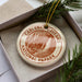 A circular ornament with the text "CARLSBAD CAVENS NATIONAL PAPARK" printed on it, placed in a box with pine branches.