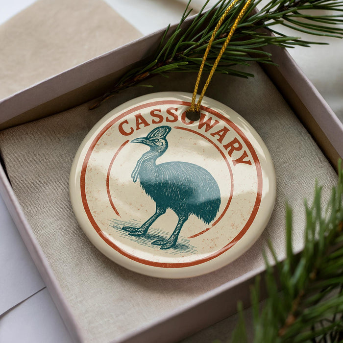 A circular ornament with a bird image and the word "CASSOWARY" written on it, placed in a box with pine branches.