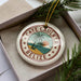 A round ornament with the text "CAYE CAULKER BELIZE" and a tropical beach scene, surrounded by pine branches.