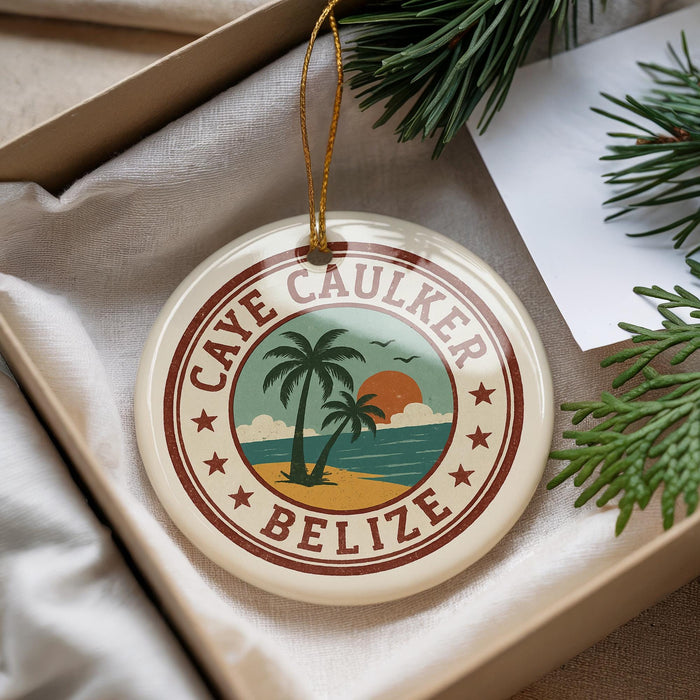 A circular ornament with the text "CAYE CAUKER BELIZE" and a palm tree design, placed on a white surface next to pine branches.