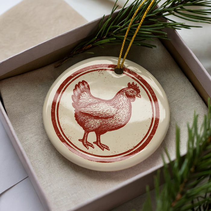 A ceramic ornament in the shape of a chicken is displayed in a box, surrounded by pine branches.