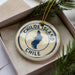 A circular ornament with the text "CHILIE" and a map of Chile, placed inside a box with pine branches.